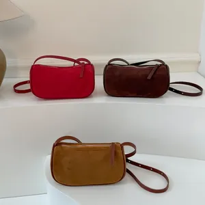 Borse a tracolla minimaliste in pelle scamosciata rossa, marrone e gialla su un piedistallo