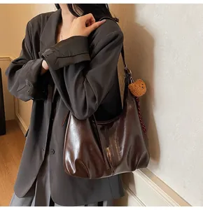 Detail view of a glossy dark brown hobo bag with a cute plush bear charm accessory