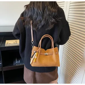 Detalle de un bolso tote de ante color jengibre con cierre de giro y amuleto de cuentas