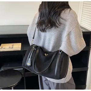 Detail of a black suede Boston bag with leather handles and gold brand tag hanging