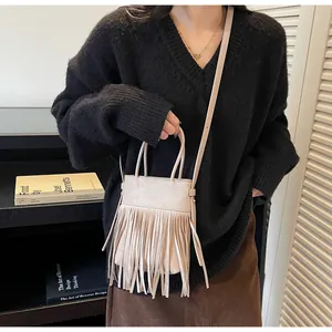 Détail d'un sac bandoulière beige à franges en suédine porté avec une tenue chic