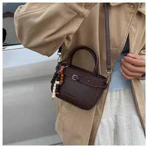 Detail of dark brown leather handbag with wooden bead charm and embossed logo