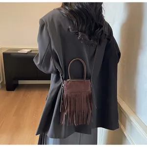 Détail d'un sac seau en daim marron foncé avec de longues franges et zip métallique
