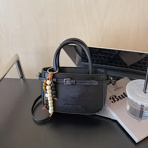 Minimalist black leather crossbody handbag with decorative buckle and beaded charm