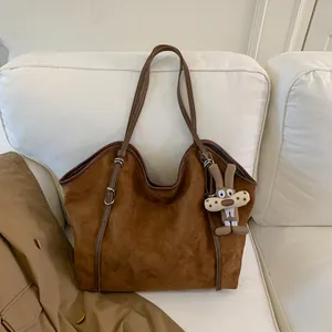 Détail d'un sac cabas en daim marron avec un porte-clé lapin en peluche sur un canapé