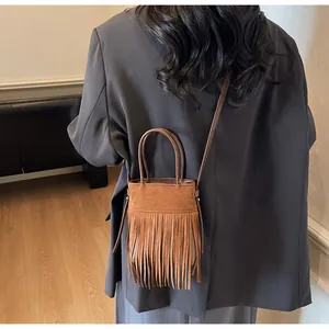 Détail d'un sac seau marron à franges avec doubles poignées porté par un mannequin