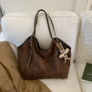 Détail d'un cabas en daim marron avec pendentif lapin à longues oreilles sur un canapé