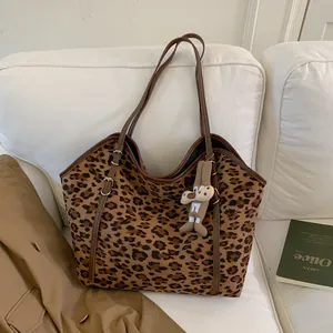 Détail du cabas léopard avec lanières en cuir marron et pendentif posé sur un canapé blanc