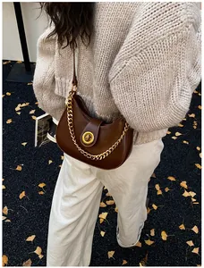 Detailed close-up of brown crescent moon bag with gold chain on autumn leaf background