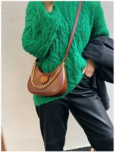 Close-up of brown crescent bag with gold chain strap on green knit sweater outfit