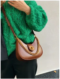 Close-up of brown half-moon shoulder bag with gold chain strap on green knit sweater