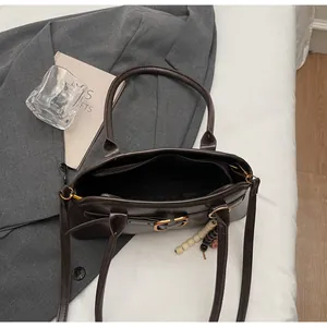 Detail of dark brown leather shoulder bag with gold clasp and decorative beads on a blazer