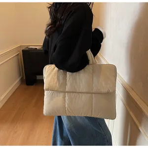 Dettaglio di una borsa tote trapuntata beige indossata da una modella in una stanza