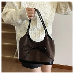 Detail of dark brown suede shoulder bag with a bow accent worn by a model in a cozy sweater
