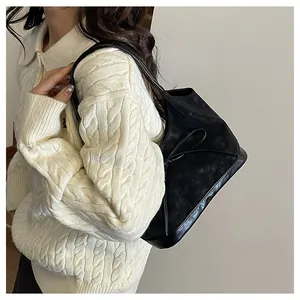 Detail of black suede shoulder bag with bow accent worn over a white knit sweater