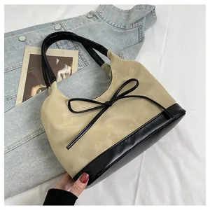 Detail of minimalist beige faux suede bucket bag with black bow tie and leather trim