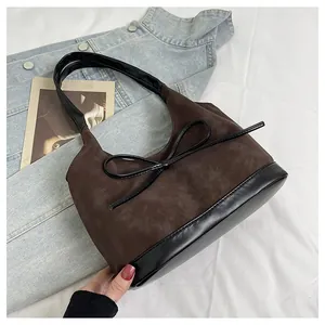 Detail of brown suede bucket bag with black leather trim and decorative bow accent