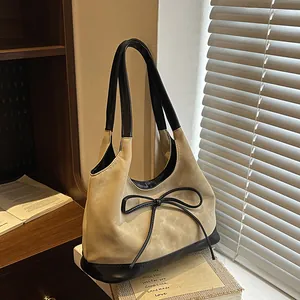 Vintage beige suede bucket bag with black bow detail shown in a cozy studio setting