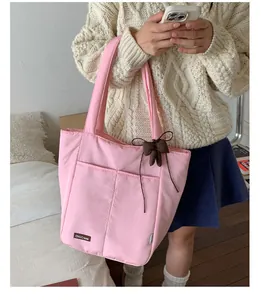 Detail of pink nylon tote bag featuring front pockets and brown bow ornament