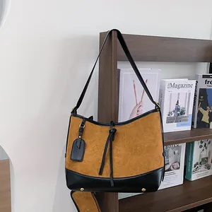 Sac hobo en daim marron avec garniture en cuir noir et bandoulière dans un décor cosy