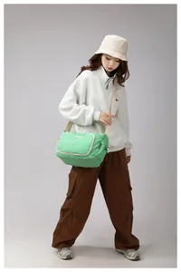 Bright green nylon messenger bag with cream strap and zip pocket shown on a model