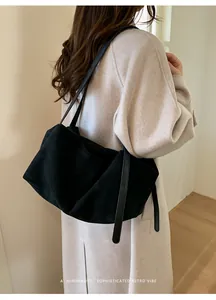Close-up of minimalist black suede tote bag with slim shoulder straps on beige coat