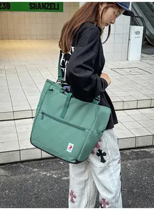 Close-up of dark green canvas tote bag featuring front zipper pocket and white brand label