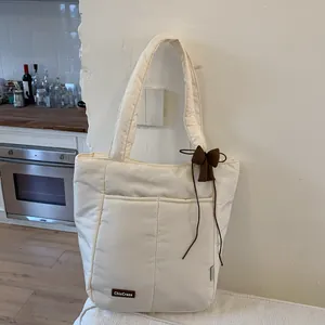 Detail of cream quilted tote bag featuring a brown leather logo and dark bow pendant