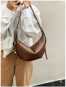 Close-up of brown leather crescent bag with wooden bead charm on a white shirt