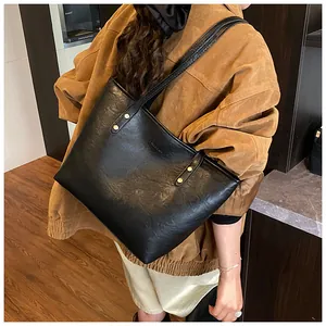 Close-up of black matte tote bag with gold rivets and brand logo on brown jacket