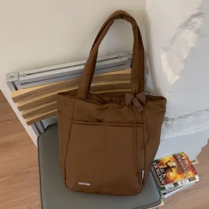 Detailed close-up of brown quilted puffer tote bag with ribbon bow and front pockets