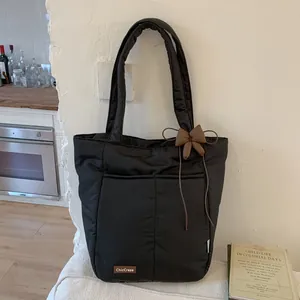 Detail of black puffy quilted tote bag with brown bow charm and leather brand tag