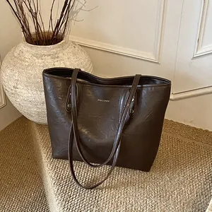 Brown leather tote bag with wrinkled texture and gold logo on a minimalist background