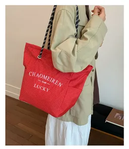 Detail of red checkered canvas tote with woven rope handle and white typography print