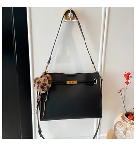 Detail of a black leather tote bag with gold metal clasp and a leopard heart pendant