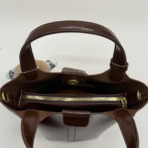 Glossy dark brown bucket bag with plush charm and golden zipper interior detail