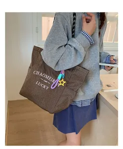 Detail of coffee plaid canvas tote bag featuring graphic text and star charm accessory