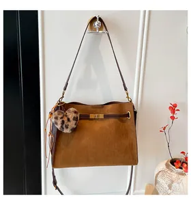 Detail of brown suede tote bag with leopard heart charm and gold buckle on a white wall