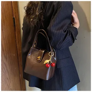 Detail of dark brown bucket bag with gold clasp and cherry charm accessory
