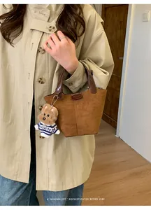 Detail view of retro brown suede handbag with leather handle and teddy bear charm