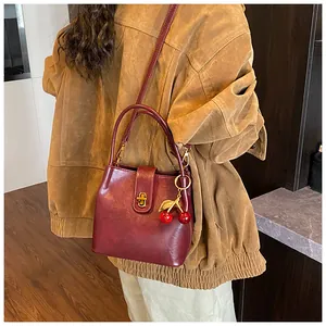 Detailed view of vintage burgundy bucket bag with cherry pendant on casual outfit