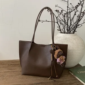 Vue latérale d'un sac cabas en cuir marron avec un charme ours et des fines bandoulières
