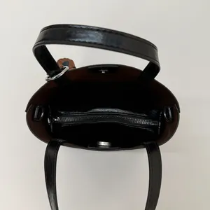 Black bucket bag with brown interior, zip pocket, and decorative leaf pendant detail