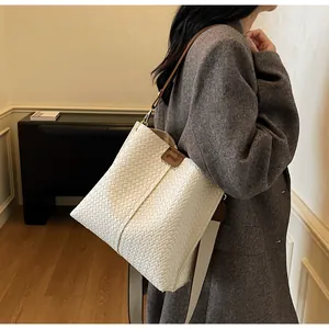Close-up of white woven texture and brown leather strap on large bucket bag