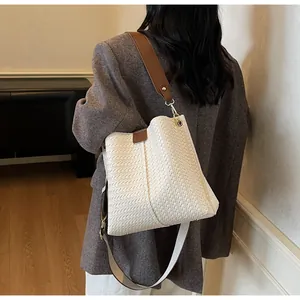 Close-up of white woven bucket bag detail with brown leather strap and gold hardware