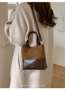 Detail of minimalist two-tone leather bucket bag with brand embossing and crossbody strap