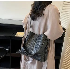 Detail shot of a black woven leather bucket bag worn with a stylish trench coat