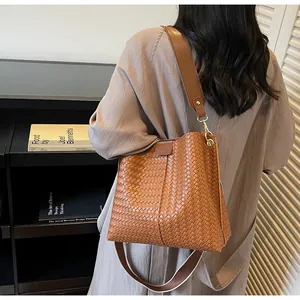 Detail of a brown woven bucket bag with leather texture and wide shoulder strap