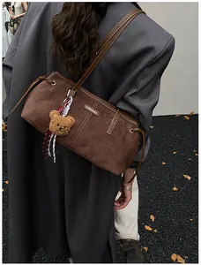 Detail view of dark brown suede tote bag with a cute plush bear pendant and metal logo