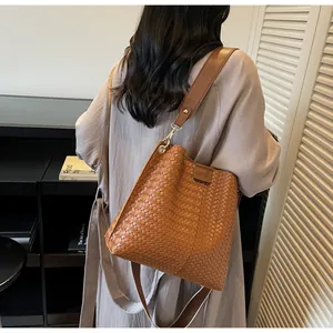 Detail of a brown woven bucket bag with wide shoulder strap and metal hardware